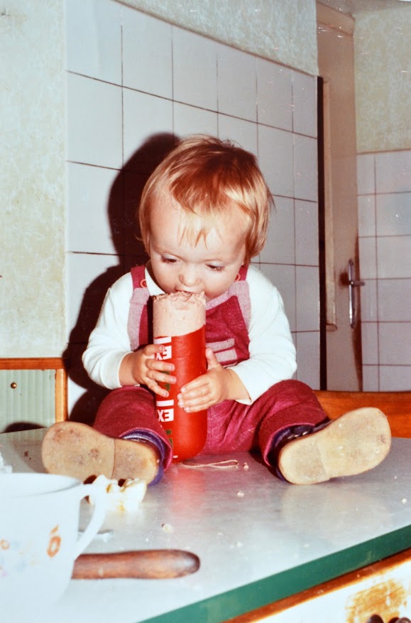 Ein Kleinkind sitzt am Küchentisch und beißt mit Genuss von einer Stange Extrawurst ab.