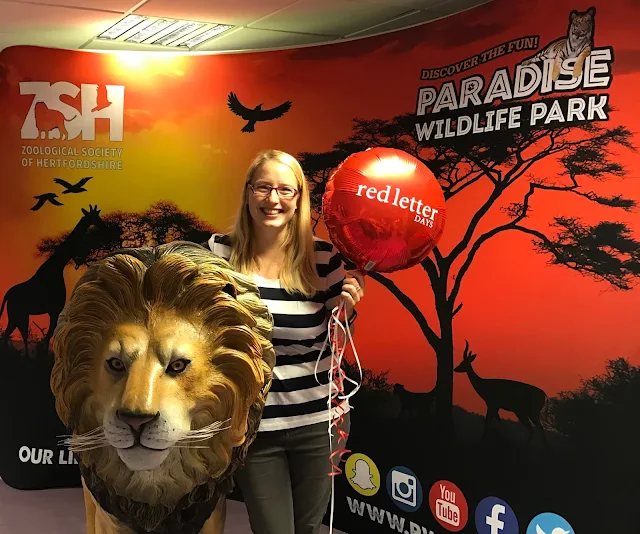 Me posing with a lion and a red balloon in front of a sign advertising Paradise Wildlife Park