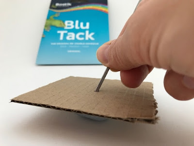Blu Tack being used to help make a hole in cardboard