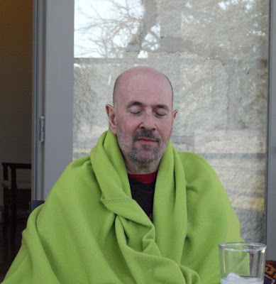 John sitting in front of a window, his eys closed, wrapped in a lime green blanket