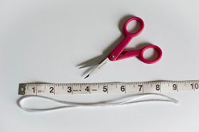 Pink scissors measuring tape and cord on white background