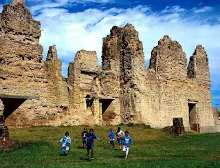 Ruinas antiguas y un grupo de niños jugando en la grama