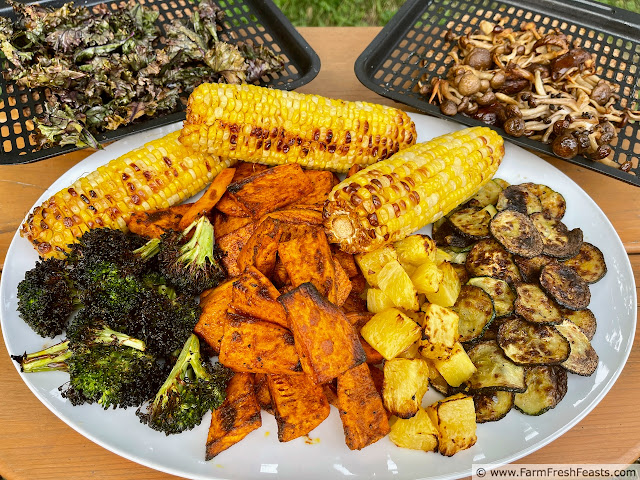 image of a plate of vegetables cooked in the air fryer (broccoli, corn on the cob, pineapple, sweet potatoes, zucchini) surrounded by air fryer trays of mushrooms and kale