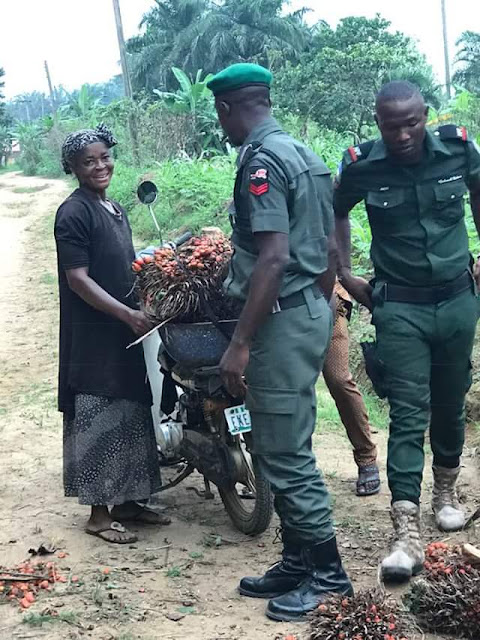  Heartwarming photos of Nigerian policemen helping an old woman tie her palm fruit bunches to a bike after they fell of