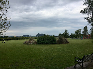 A grassy field with Holyrood Park in the distance on a cloudy day.