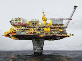 The photo shows a large oil production platform in the ocean. The platform is surrounded by several smaller vessels, probably service and supply vessels.