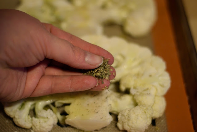 The cauliflower steaks being seasoned with Italian seasoning. 