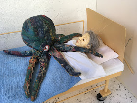 Octopus puppet on puppet in hospital bed, pinning her down, taking away her voice