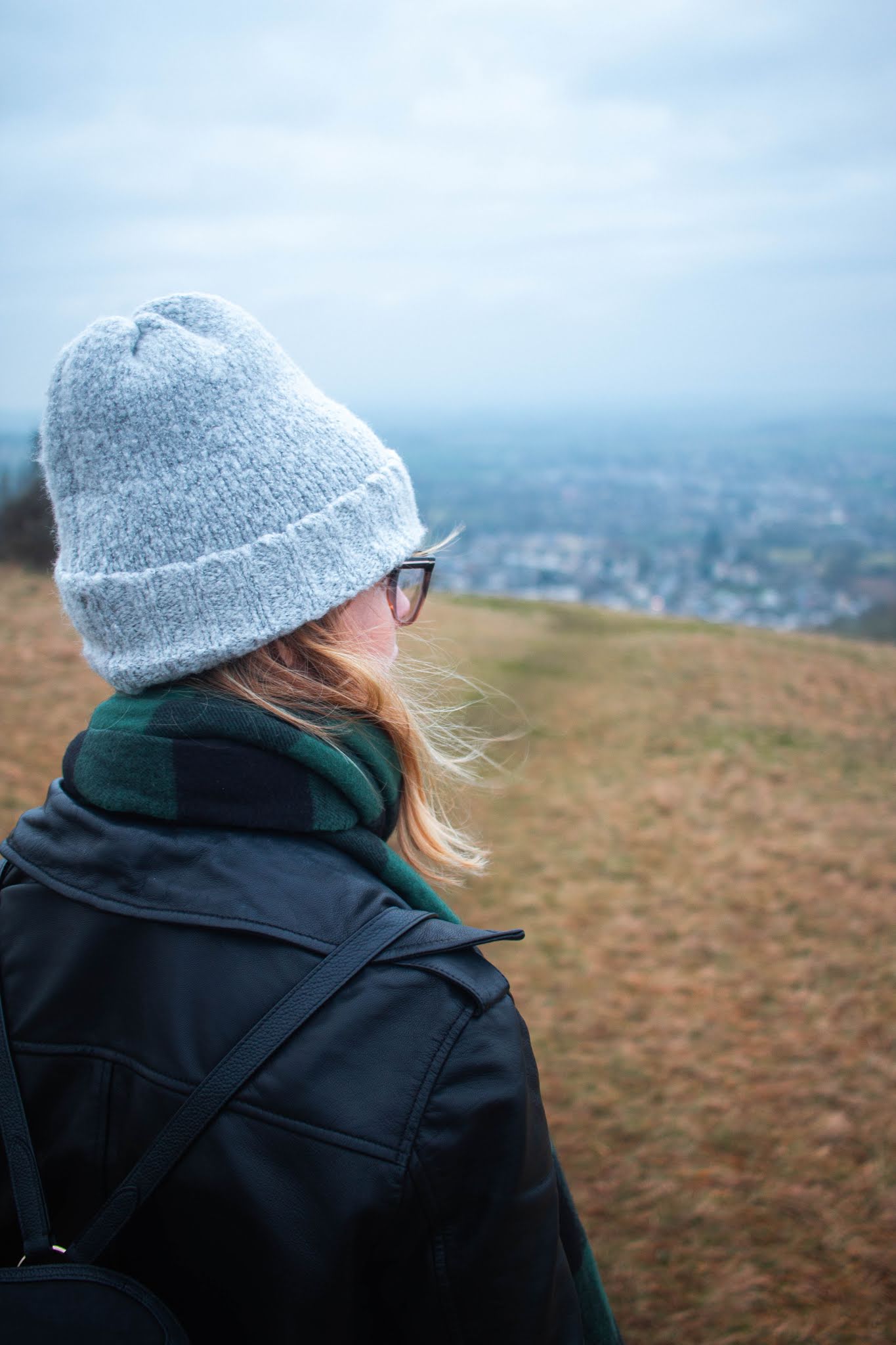 chloe harriets wearing grey beanie hat, and leather jacket looks out to scenic view - 2020 bucket list