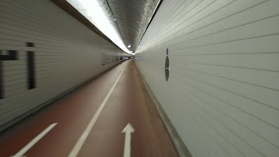 A two way red cycle track in a tunnel clad with white tiles.