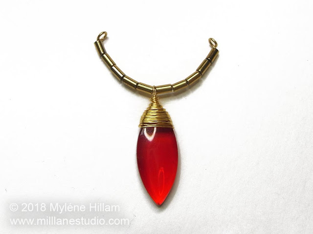 A beaded scallop component with a red dangle drop.