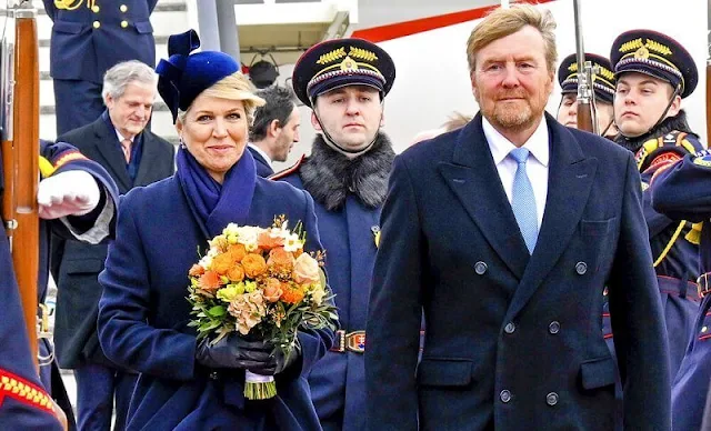 Queen Maxima's outfit, navy coat and dress, is from the fashion house Natan. Philip Treacy. President Zuzana Caputova