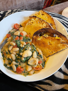 A bowl of food. On one side, crusty toasted bread. On the other, a pilaff butterbeans with tomatoes, spinach, and sauce.