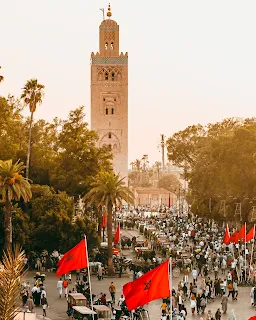 The tall minaret of the Koutoubia Mosque, Marrakech and street procession with national flag bearers in celebration.