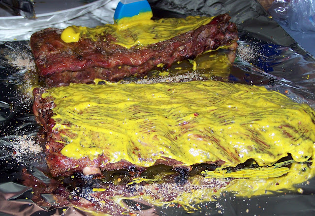 Two racks of cooked ribs being slathered with mustard