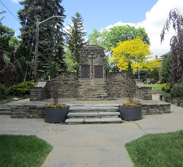 Memorial assembled from cut stone blocks. Central pillar features two plaques and a bronze sword.