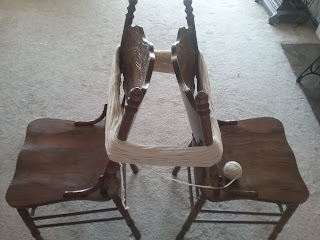 Two chairs placed back to back, a couple inches apart, holding a large skein of white around the backs.