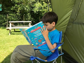 Child reading book outside tent in the shade