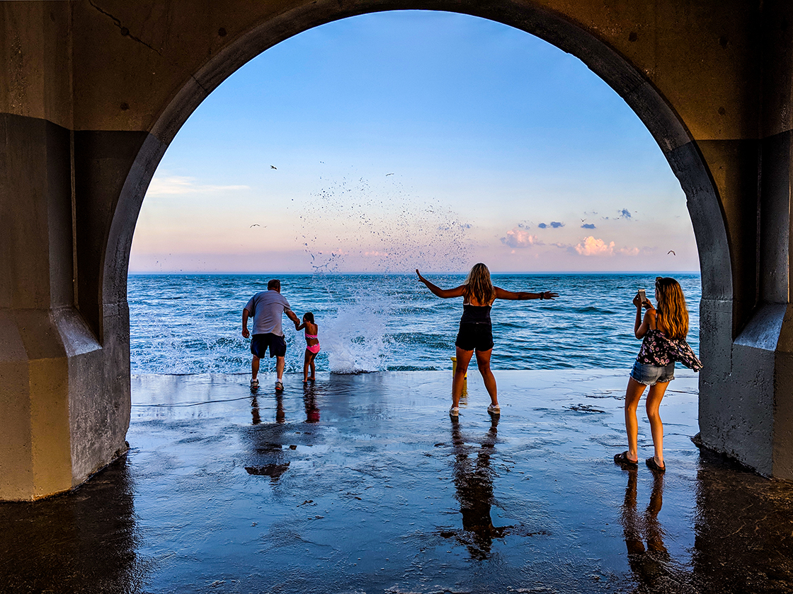 group standing on edge of breakwater being sprayed with waves