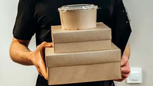 a man wearing black dress holding three brown boxes