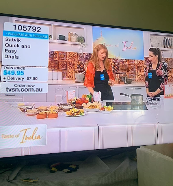 A fan's snapshot of their TV screen while watching Rada from Satvik Foods on the shopping channel TVSN. Rada is showcasing the company's range of healthy and nutritious products, including spiced dhals, rice, and organic quinoa with unique Ayurvedic spice blends. The viewer is enjoying the segment from the comfort of their own home and getting a glimpse of the delicious offerings from Satvik Foods