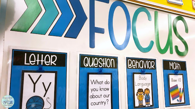 "Focus" written in large letters on a white board, 4 posters underneath  listing objectives for: letter, essential question, behavior, and math