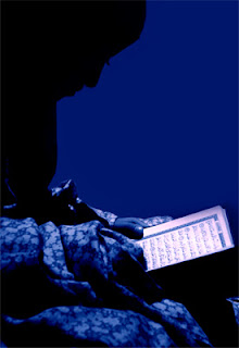 A girl is profiled against a backdrop of blue, her head bent over a Koran.