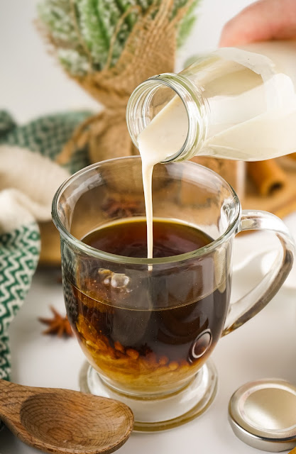 creamer being poured into a glass mug of coffee.