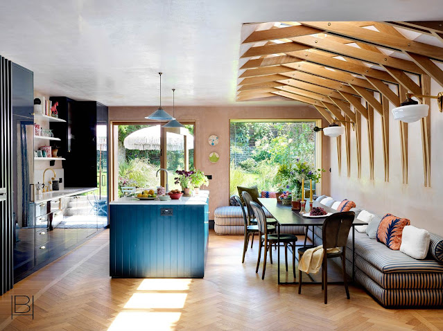 Beata Heuman kitchen and eat in dining room with blue striped lounging sofa banquette seating, shiny blue kitchen cabinets, and modern wood ceiling beam detail