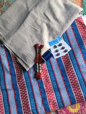 Two hanks of red embroidery floss, a spool of navy thread, and two cards of three silver shank buttons each stacked on a folded piece of off-white dotted fabric and a larger folded piece of red, blue, and white patterned striped fabric.