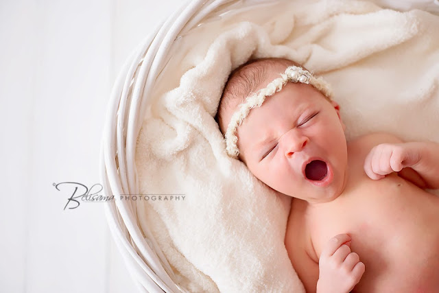 beautiful baby girl yawning in white basket on white wood floor