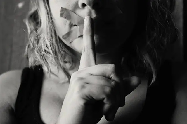 An image of girl with a cross on her mouth and finger on her lips in the grey background- sad girl dp