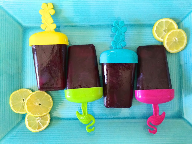 Blueberry Lemonade Popsicles laying on a teal serving platter with fresh slices of lemon