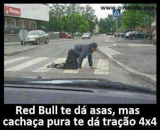 Foto tirada de dentro de um veículo em uma rua com poucos carros. Um homem engatinhando, atravessa na faixa de pedestres. Abaixo a frase: Red Bull te dá asas, mas cachaça pura te dá tração 4X4.  