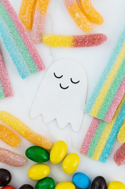 ghost cut-outn on white background with a cute face surrounded by candies.