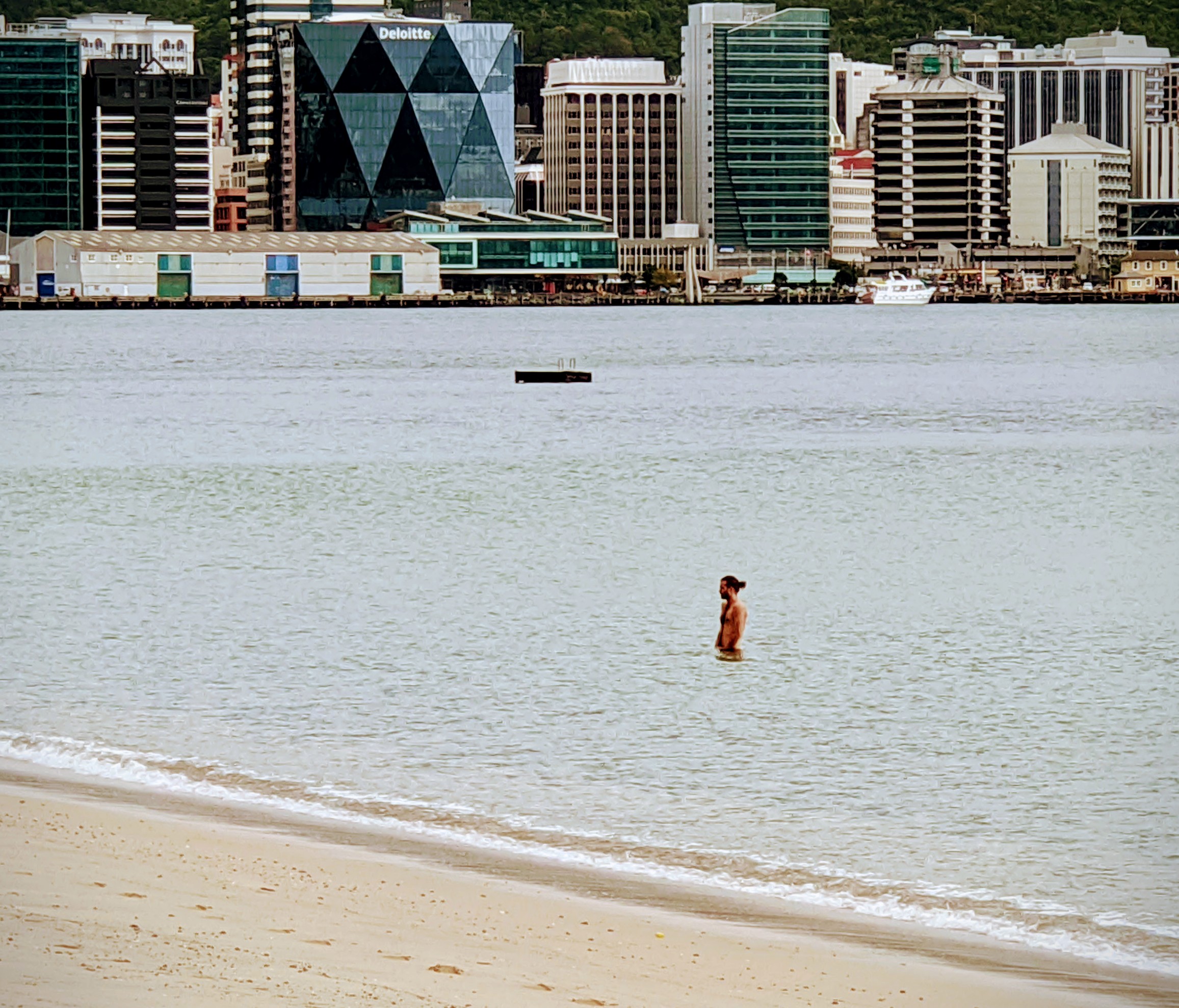 A man, alone, in Wellington Harbour with the CBD in the background