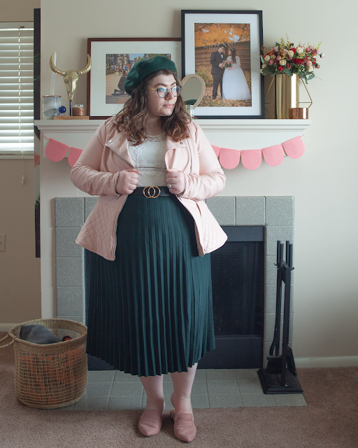 An outfit consisting of a green beret, pastel pink faux leather in a quilted peplum cut over a lace blouse tucked into a forest green pleated midi skirt and dusty pink pointed toe mules.