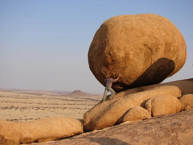 A man is holding a huge boulder in place symbolising hard-work and strength