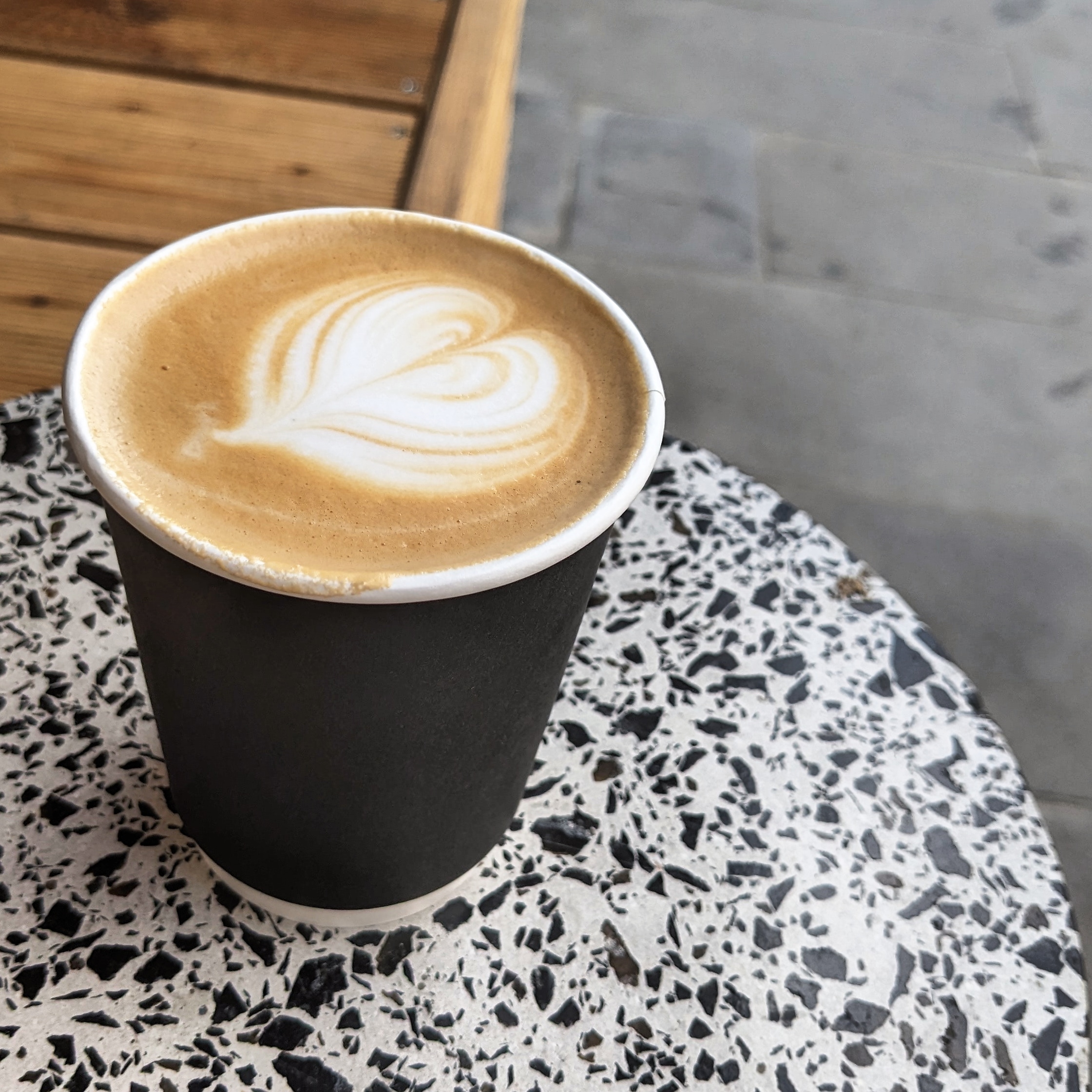 A flat white coffee in a black paper cup on a terrazzo tile table outside Pro Barista coffee shop in Tbilisi, Pro Barista is one of the best cafes in Tbilisi