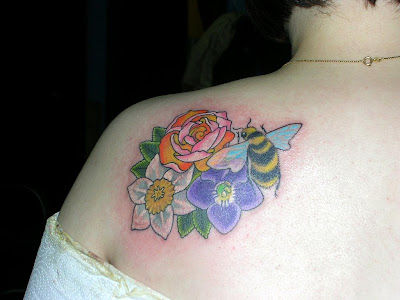 A nice and colorful back of shoulder tattoo of flowers with a bee resting on 