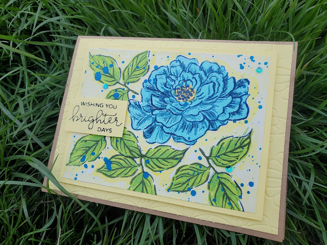 Blue Peony hand made greeting card with bright blue ink splatters and three blue sequins mounted on a yellow card base. The sentiment reads "wishing you brighter days". The card is sitting in green spring grass.