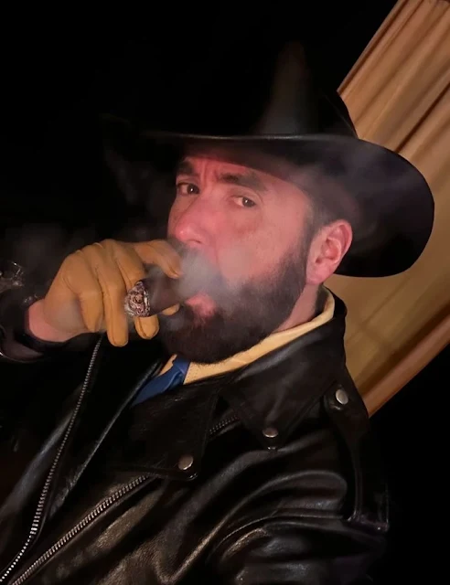 Cigar smoking cowboy wearing black heather biker jacket with orange gloves