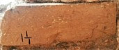Εικ. 8α–β. Βόρεια εξωτερική όψη - επικλινής κατασκευή.  Κατεργασμένος λίθος με αρχικά λιθοξόου (συλλαβικό Ε) απόδοση Άρτεμης Καρναβα