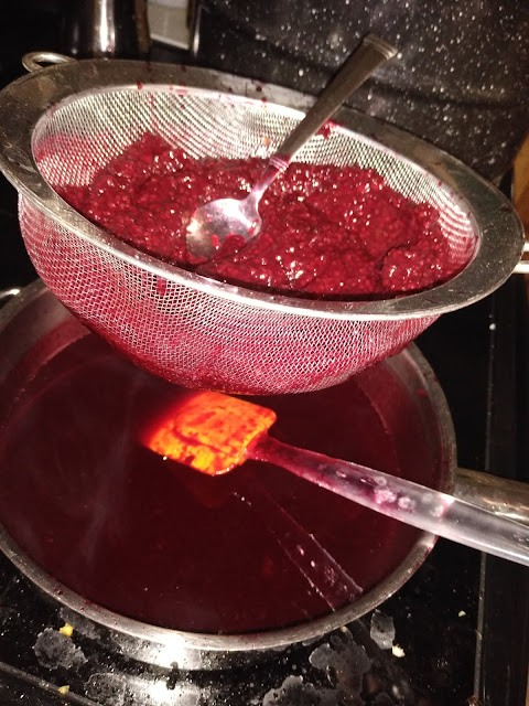 Using a strainer to remove the blackberry basil syrup from the pulpy mash