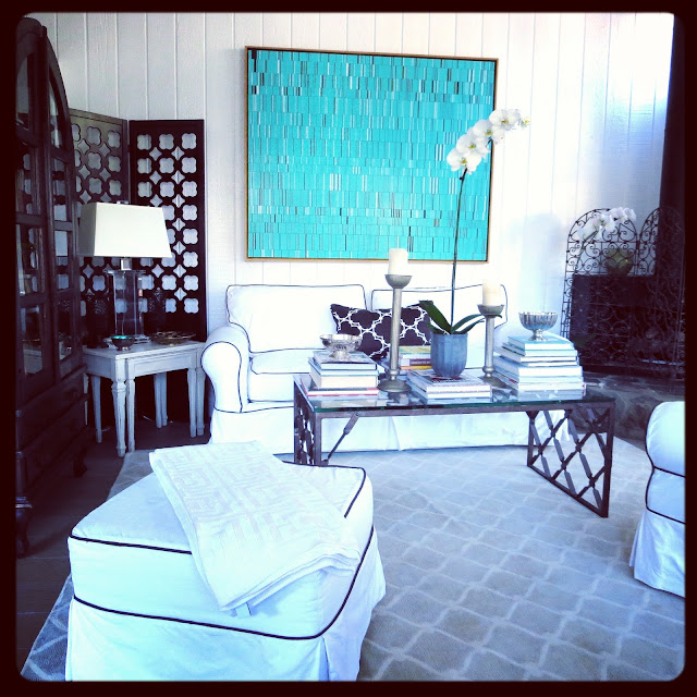 Turquoise piece by Brian Wills in Coco of COCOCOZY's living room with a white sofa and matching armchair and ottoman with brown piping and a COCOCOZY Fence rug