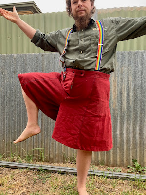 A white person with dark hair models a pair of knee length,  red culottes. They are standing on one leg, with the other raised to hip height with the knee bent, to show the range of motion allowed by the culottes. End ID.