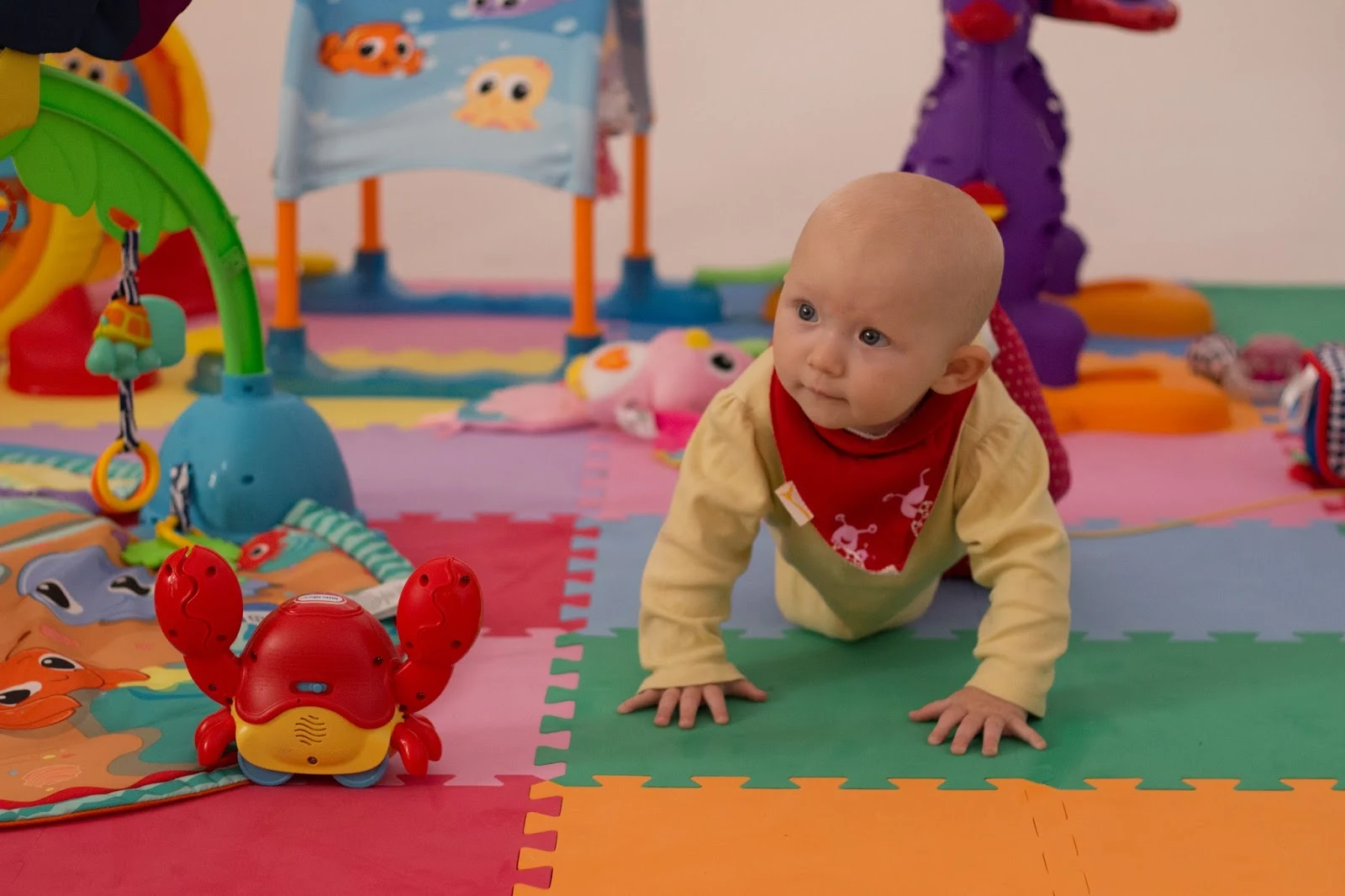 A baby crawling surrounded by Little Tikes toys on brightly coloured mats