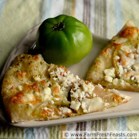 a close up image of green tomato pizza with pesto and feta cheese