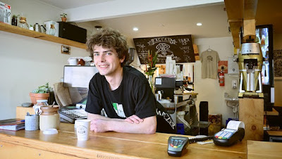 man in black t shirt smiles from behind a counter