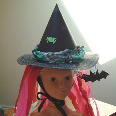 A witches hat made out of two sheets of A3 black card and decorated with crepe paper, scrap fabric, stickers and white pencil.